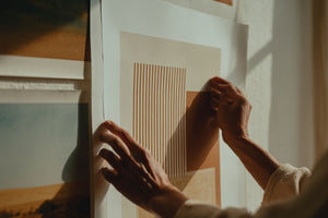 Person hängt minimalistisches Poster mit geometrischen Linien an weiße Wohnzimmerwand auf