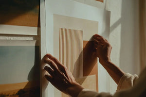 Person hängt minimalistisches Poster mit geometrischen Linien an weiße Wohnzimmerwand auf