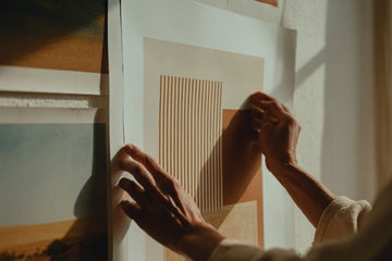 Person hängt minimalistisches Poster mit geometrischen Linien an weiße Wohnzimmerwand auf